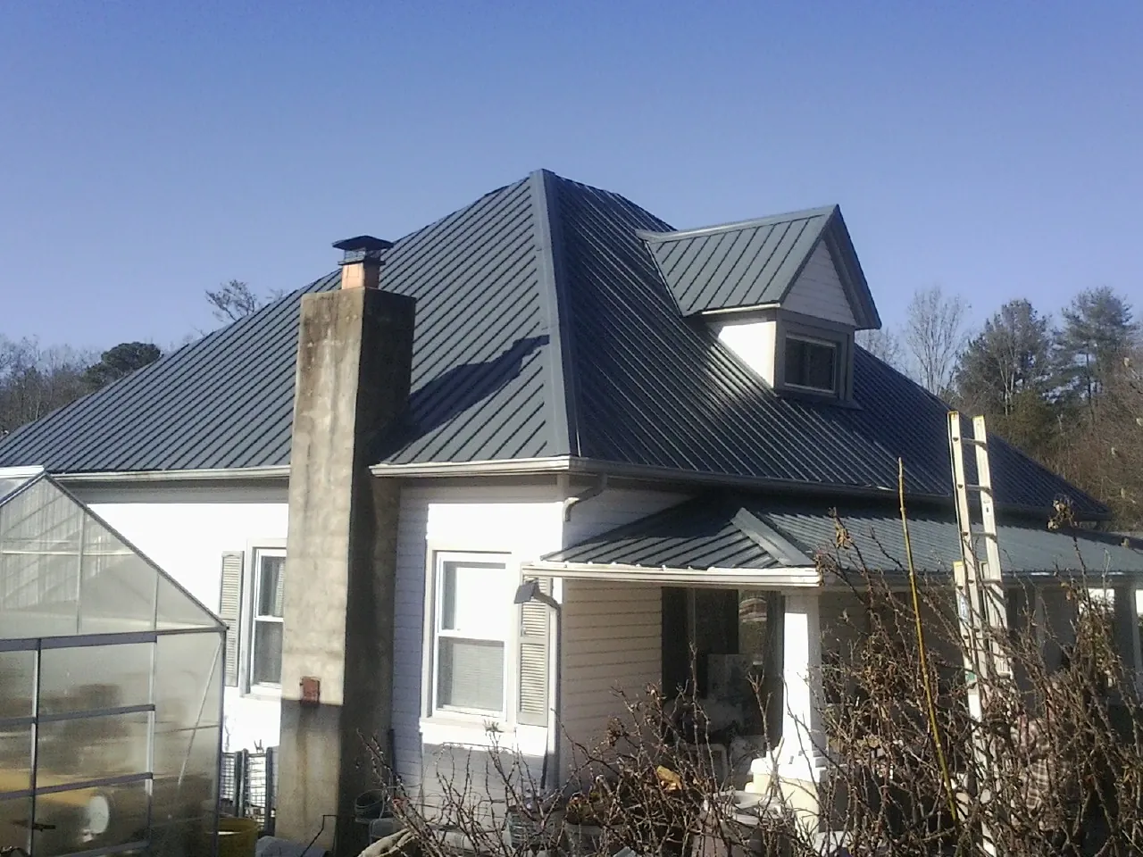Dark blue standing seam metal roof on a white farmhouse with dormer — Slate & Tile Roof Repair by Roofing Brothers in Matheson
