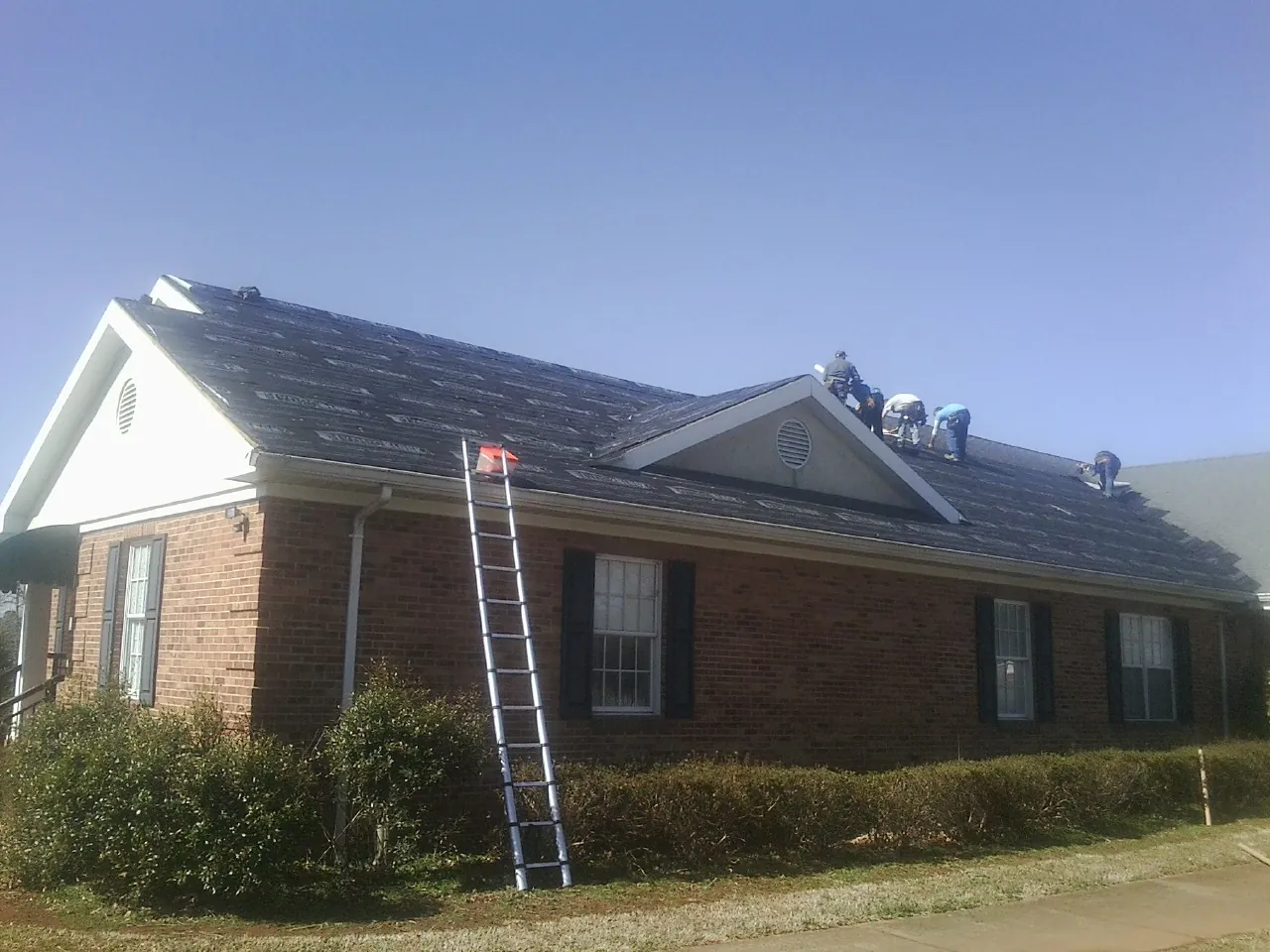 Crew tearing shingles off a brick ranch roof with a ladder set — Emergency Roof Repair work by our crew in Matheson
