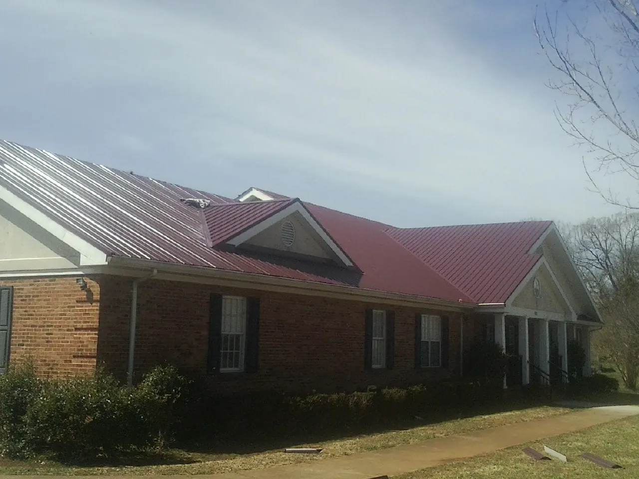 Red metal roof with gabled entries on a long brick building, from a Hail Damage Roof Repair job in Matheson