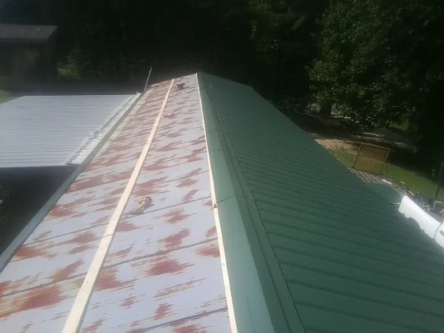 Old rusted panels beside newly installed green metal roofing — Wind Damage Roof Repair by Roofing Brothers in Matheson