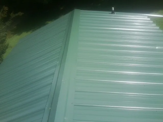 New green metal panels meeting at the ridge of a roof — Flat Roof Repair work by our crew in Matheson