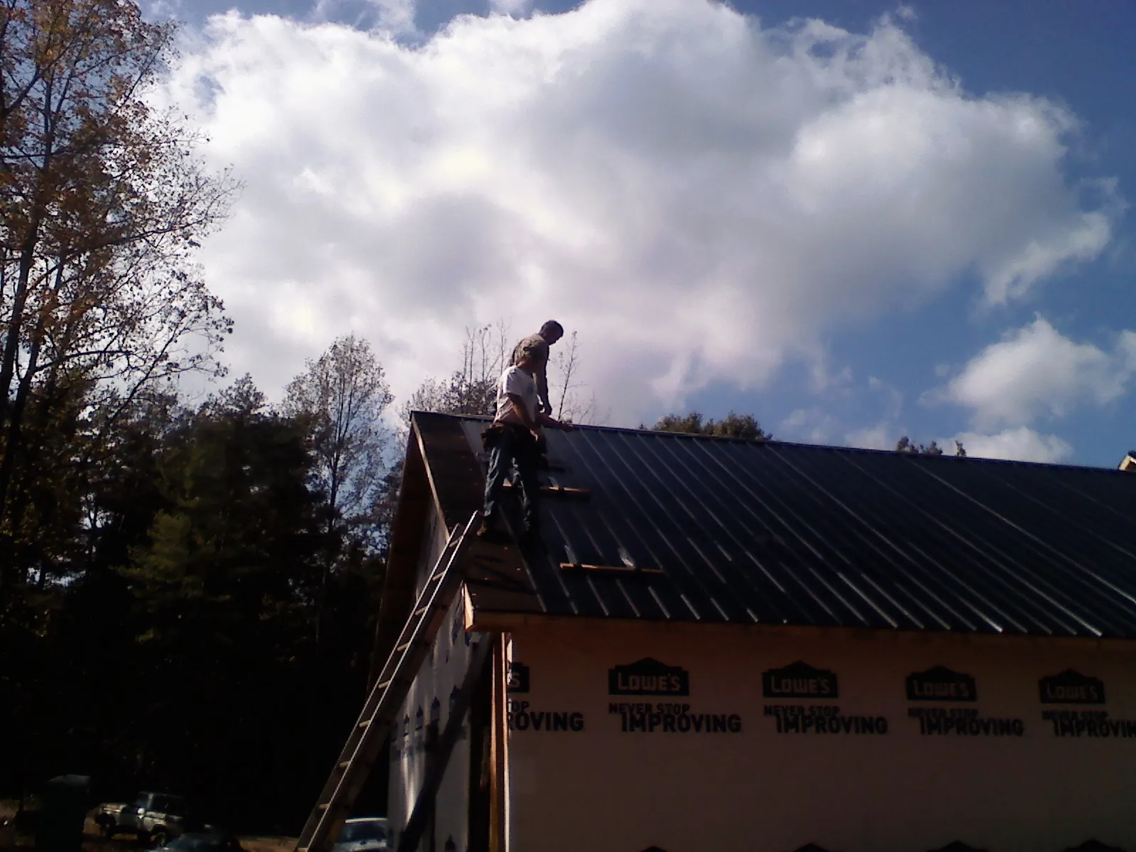 Roofer fastening dark metal panels high against a cloudy sky, from a Roof Inspection job in Matheson