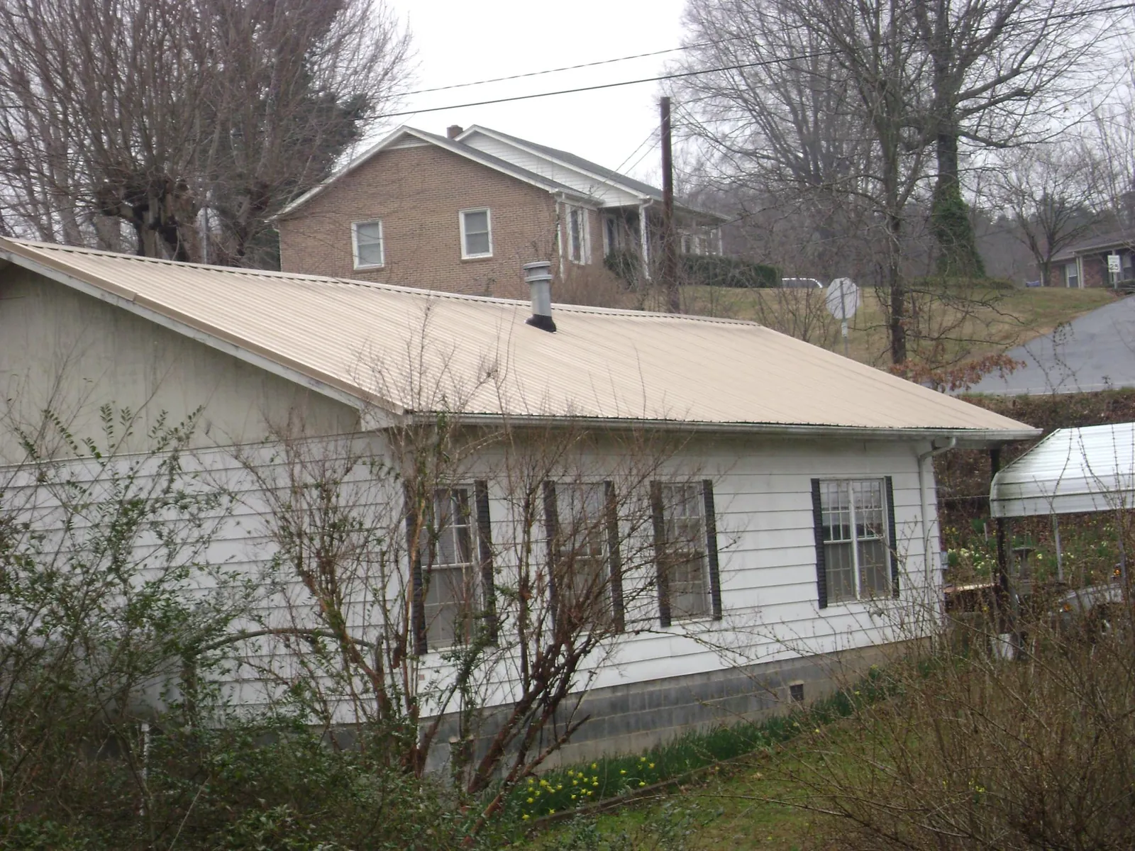 Tan metal roof on a white sided house set into a hillside — Commercial Roofing by Roofing Brothers in Matheson