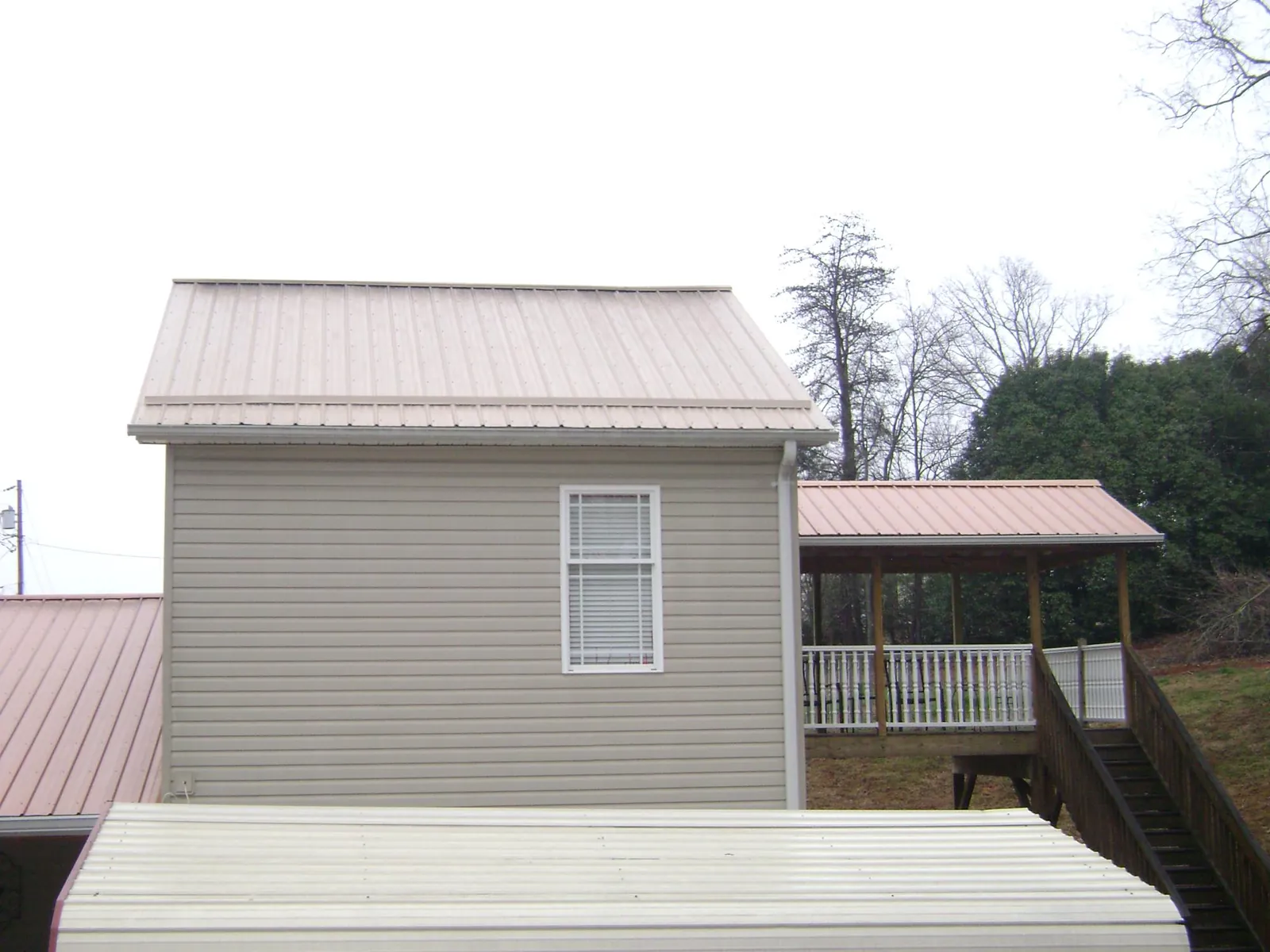Tan metal roofs on a two story addition and attached porch, from a Roof Replacement job in Matheson
